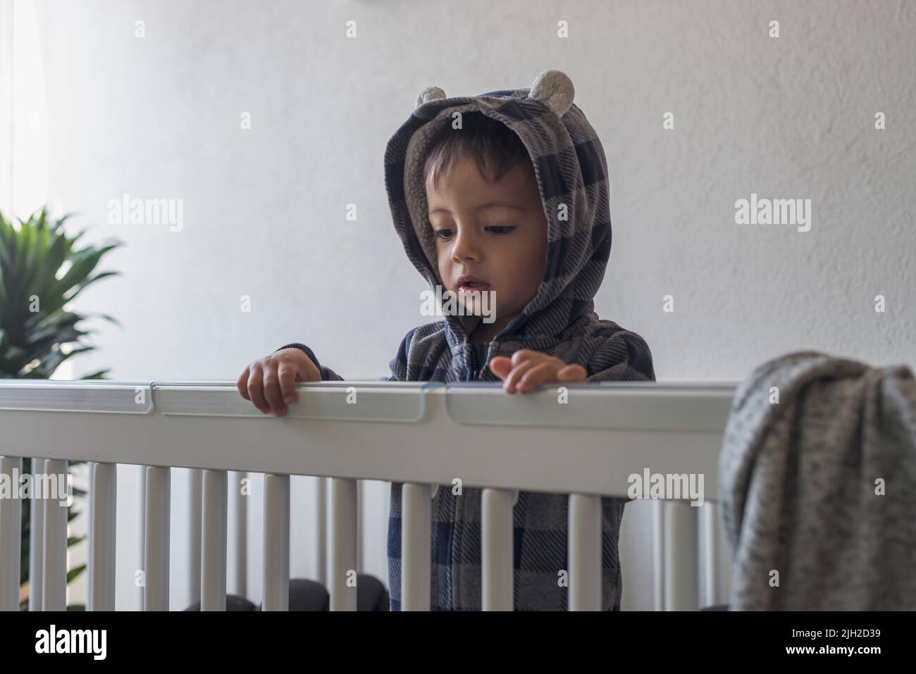 Carino bambino latino in piedi nella sua culla con un cappuccio Foto Stock