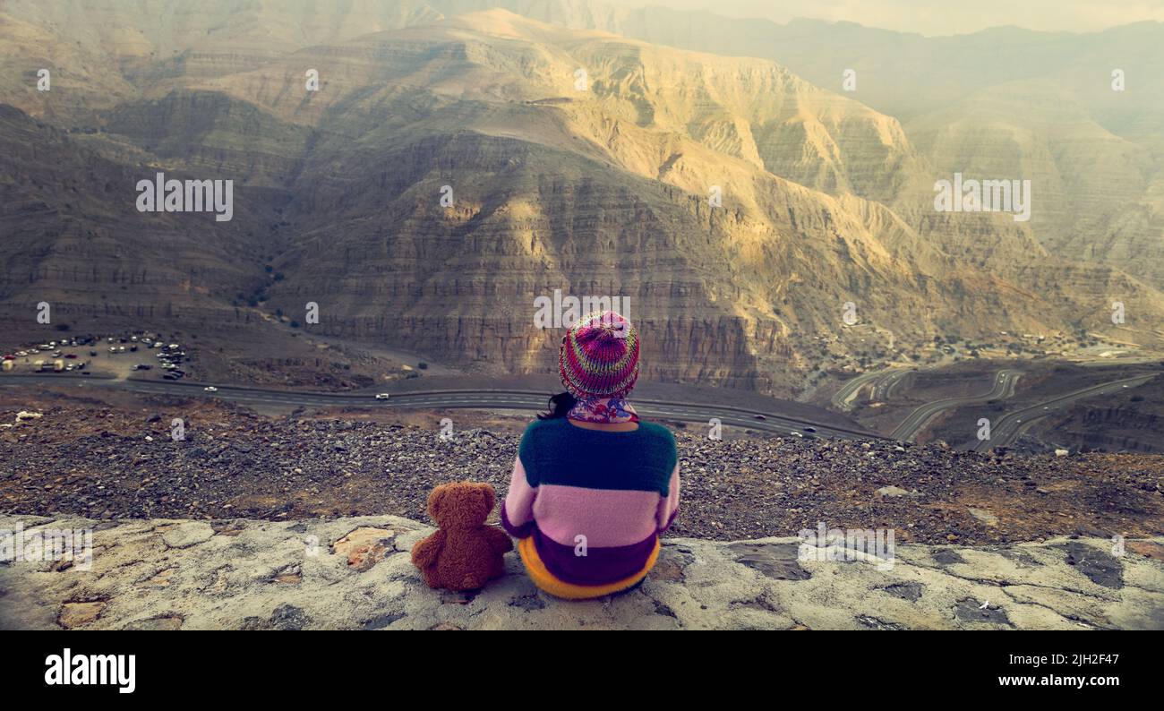 Giovane ragazza con un orsacchiotto seduto in cima alla montagna guardando la valle in Jabel Jais, Ras al Khaimah, Emirati Arabi Uniti Foto Stock