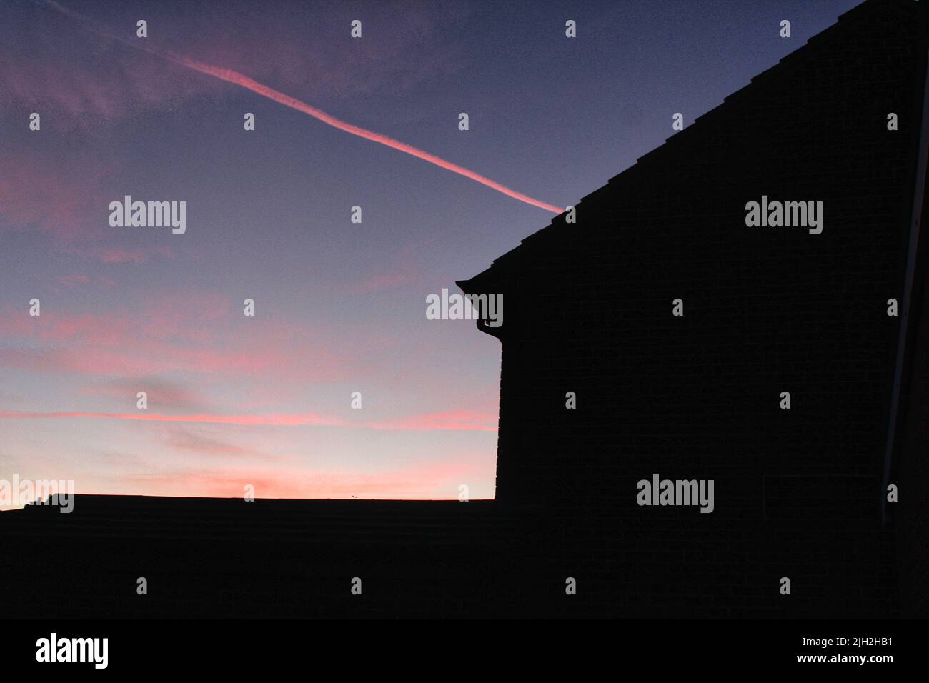 Cielo al tramonto viola e rosa dietro una silhouette di una casa. Foto Stock