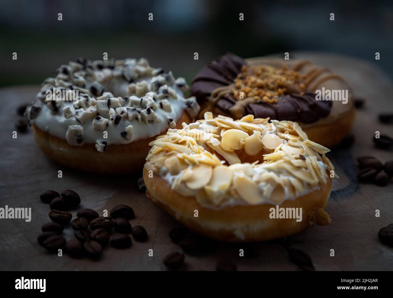 Tre ciambelle ricoperte di Almendras, biscotti e crema e burro di arachidi al cioccolato su tagliere di legno. Il concetto di deliziose ciambelle glassate, Spa Foto Stock