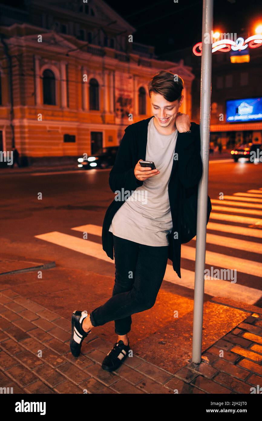 Ragazzo sorridente con smartphone nella città notturna Foto Stock