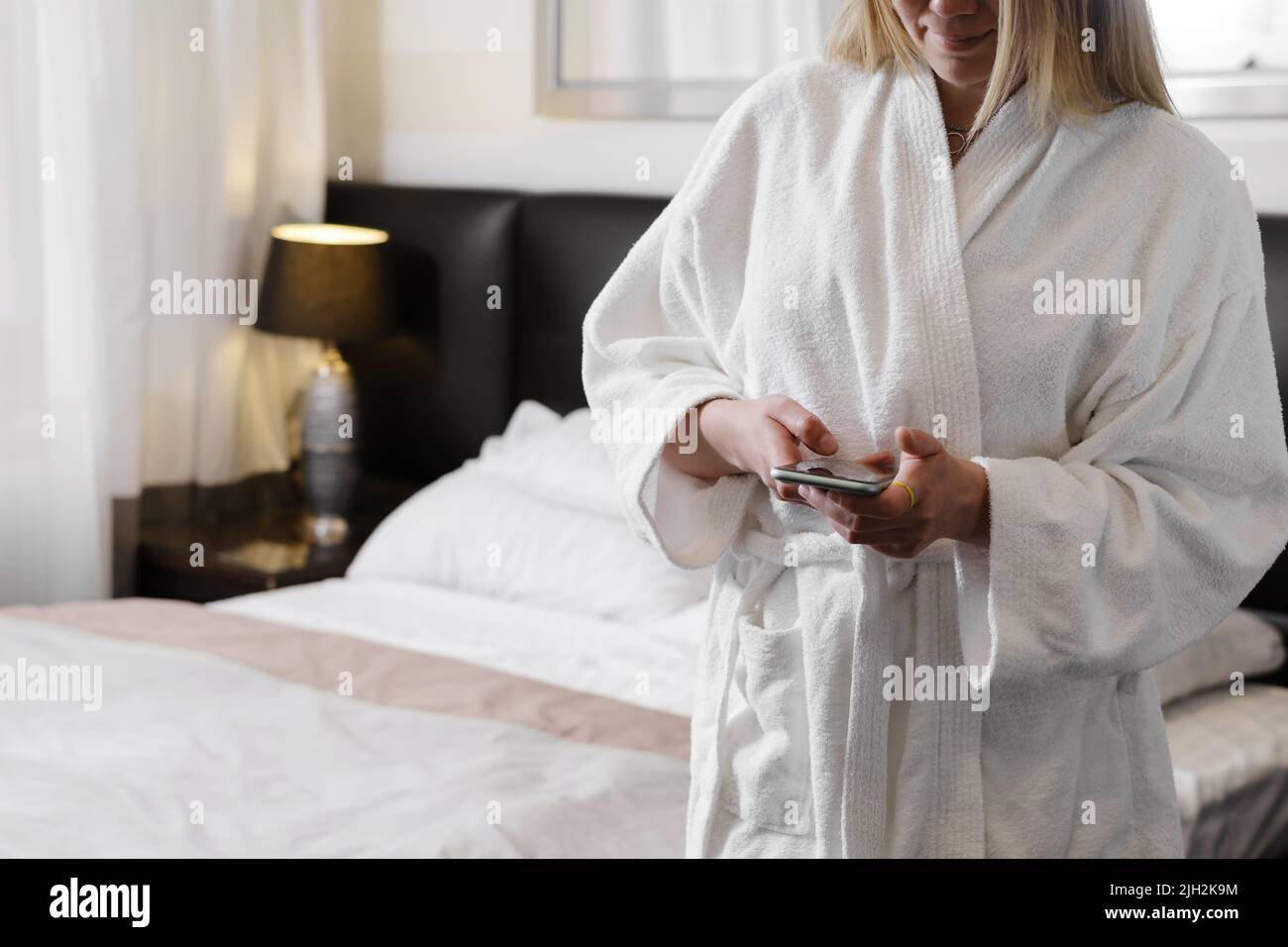 Donna che indossa l'accappatoio mentre si trova in camera d'albergo utilizzando lo smartphone. Comunicazione, servizio di ordinazione, shopping on-line durante il viaggio. Persona in Foto Stock