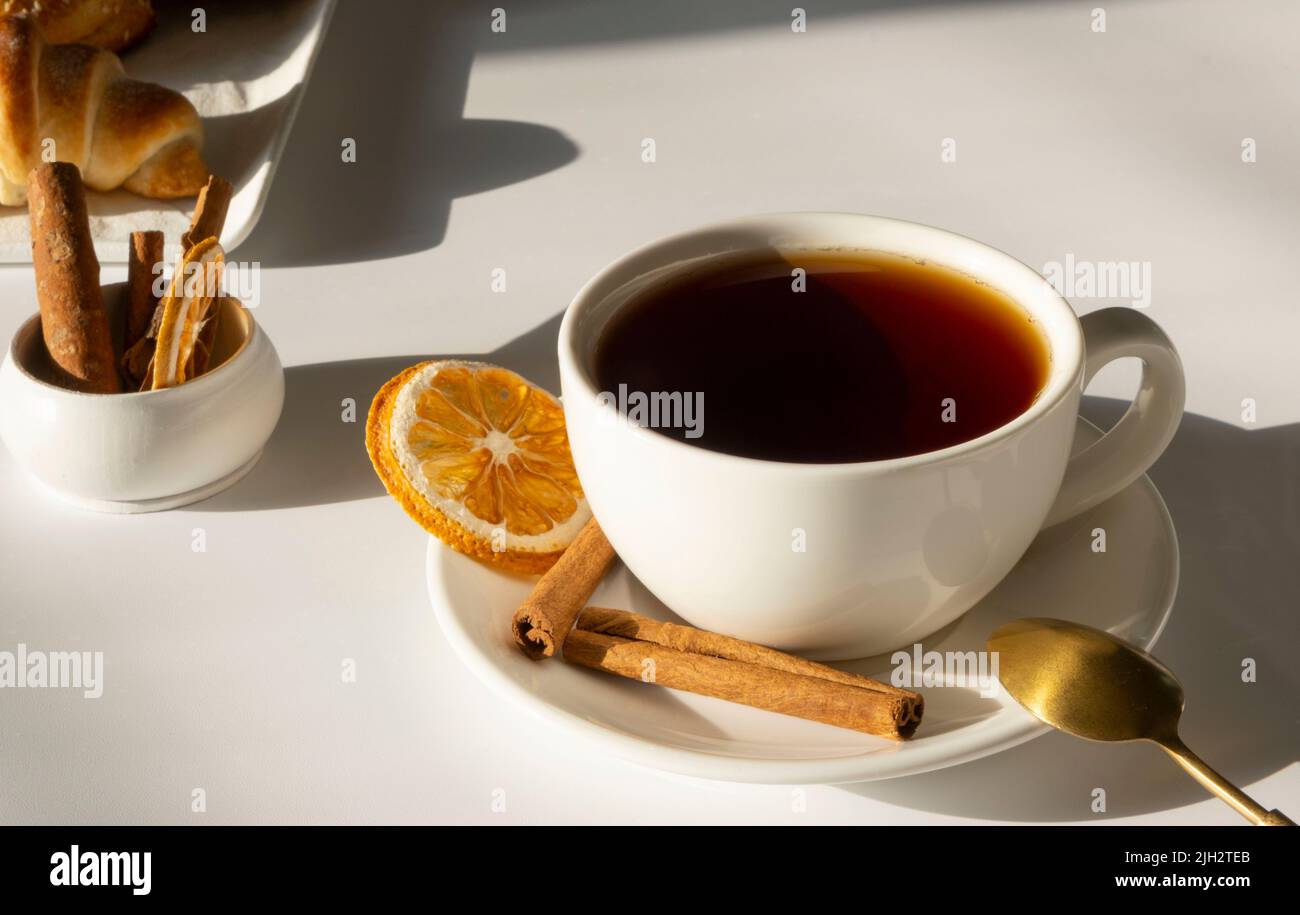 tè nella tazza bianca o in una tazza su sfondo bianco e chiaro con dolci freschi e croissant, colazione o concetto di mattina Foto Stock