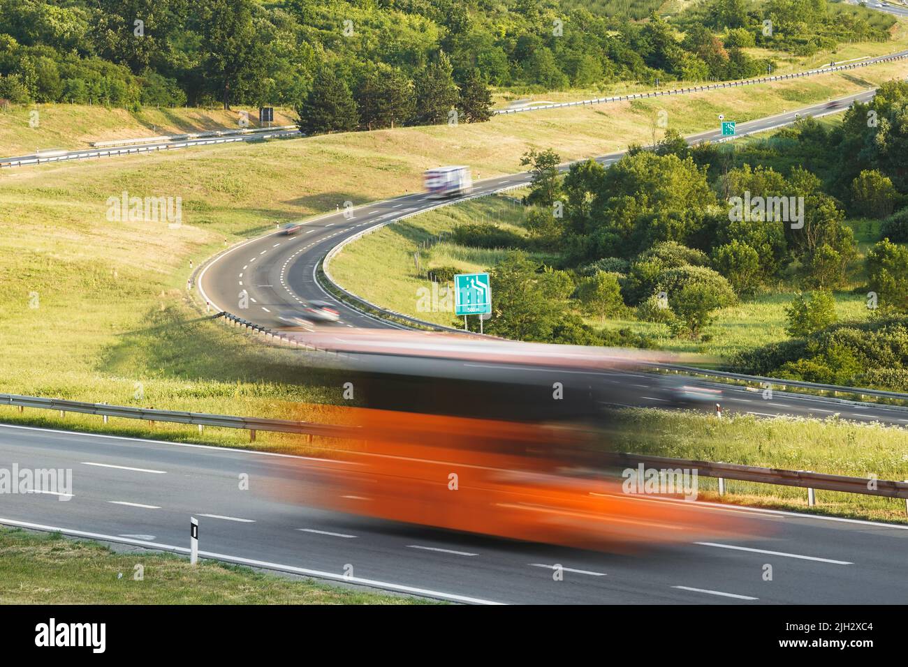 Guida veloce sulla superstrada in un bellissimo paesaggio. Camion di consegna blurred veloce e automobili sull'autostrada, ora del tramonto Foto Stock
