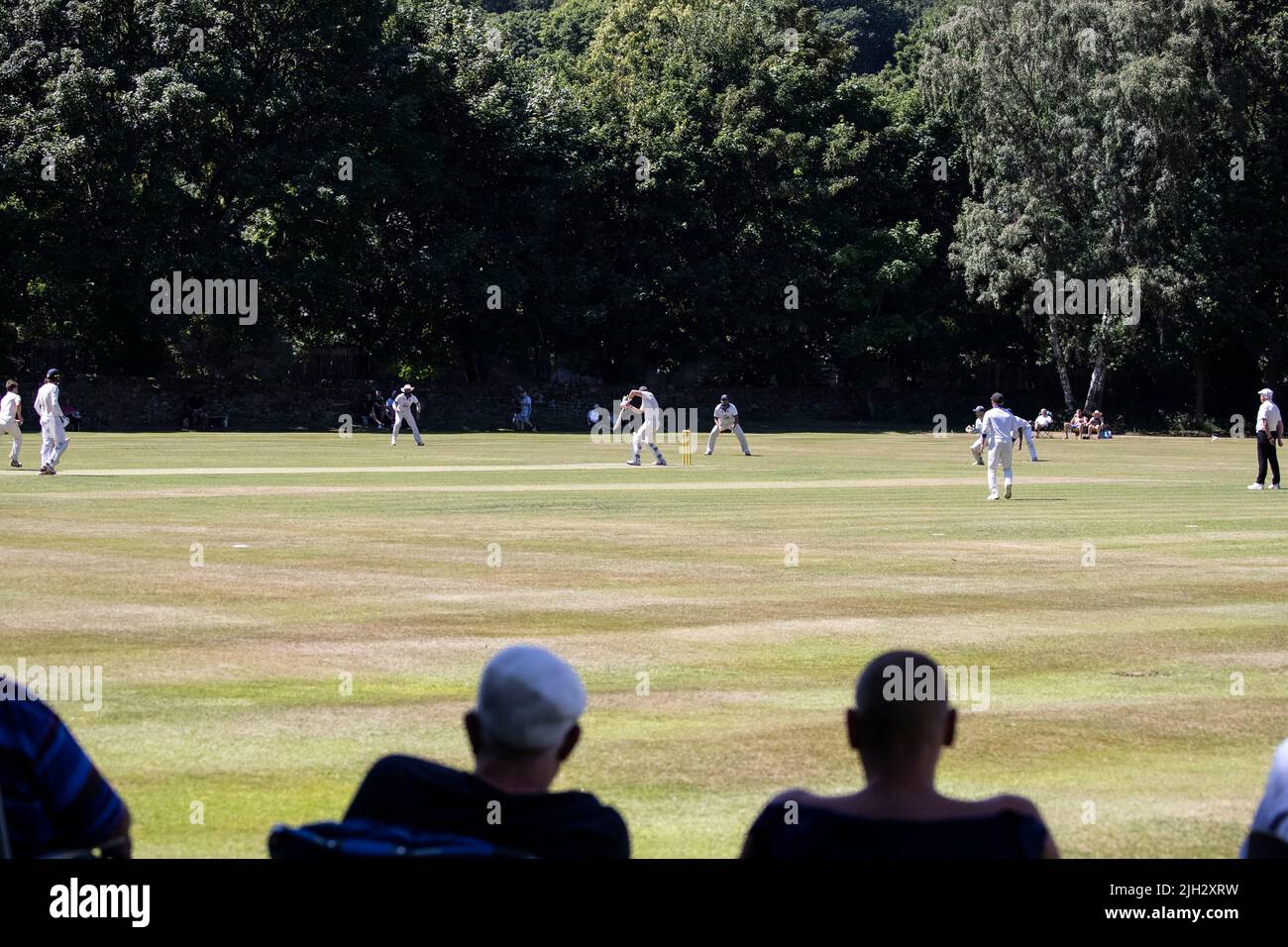 Village Cricket partita essere guardato da spettatori interessati su un bel terreno alberato a metà estate nel West Yorkshire Foto Stock