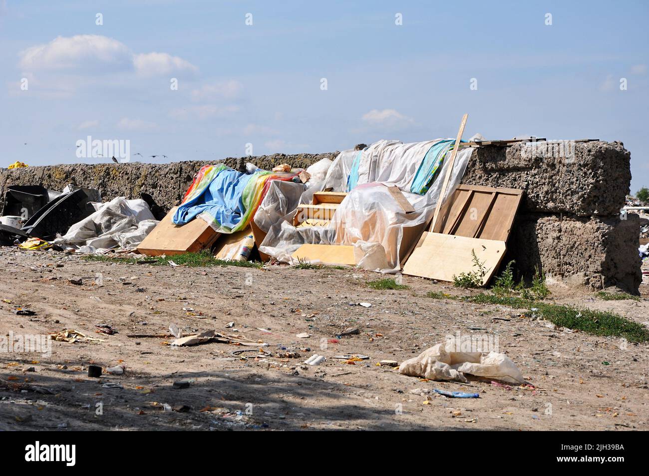 Mobili antichi e tela di scarto in una discarica comunale vicino a muro in rovina in giorno di sole Foto Stock