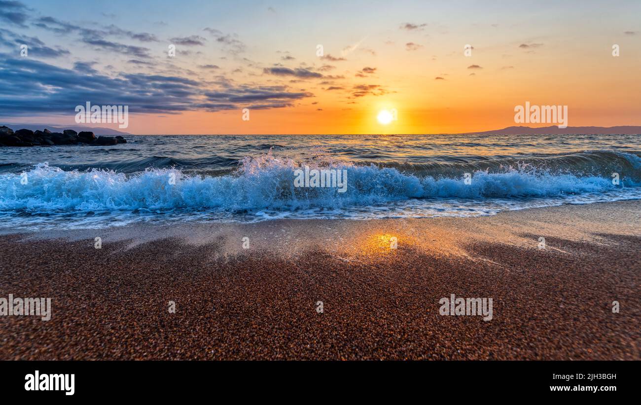 Il sole sorge come un'onda spruzza su Una colorata spiaggia tropicale ad alta risoluzione Foto Stock