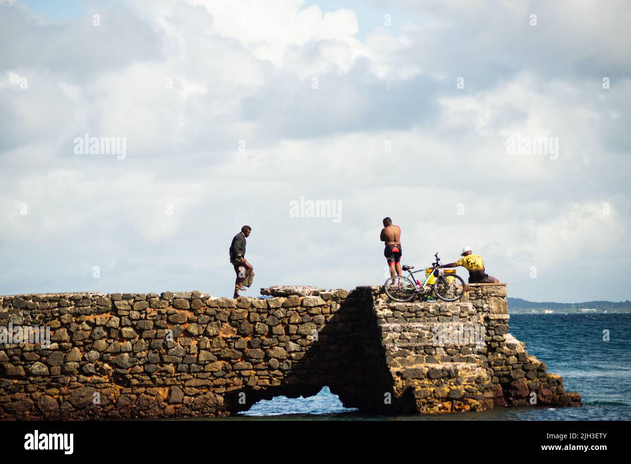 La gente cammina sulla cima del frangiflutti di pietra della spiaggia di Porto da barra a Salvador, Bahia. Foto Stock