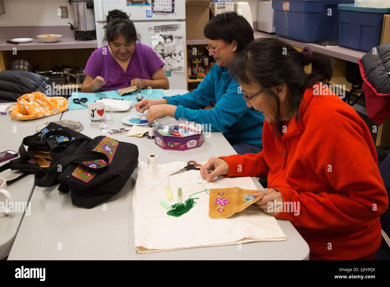 Le donne di Dene in cerchio di cucito, che si aggirano sulla pelle di moosehide tradizionalmente conciata, nella comunità indigena settentrionale di Deline, territori nordoccidentali, Canada Foto Stock