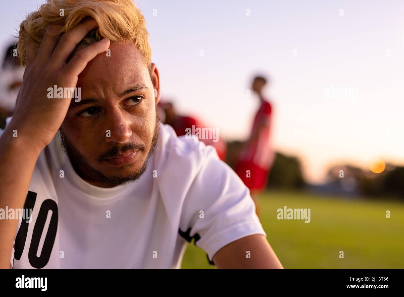 Caucasico ha sottolineato giocatore di calcio maschile con testa in mano seduta contro il cielo limpido al parco giochi Foto Stock