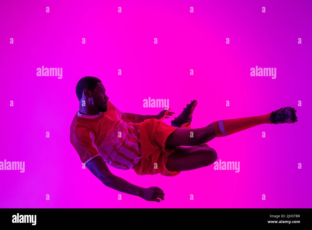 Giocatore di calcio maschile africano americano che salta su luci rosa neon Foto Stock Giocatore di calcio maschile africano americano che salta su luci rosa neon Foto Stock