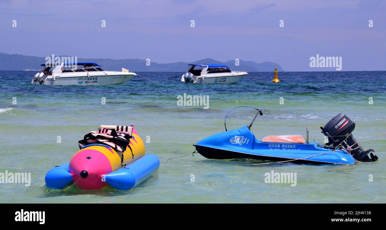 Barche a motore, un jetski e una banana boat aspettano di essere utilizzati, galleggiando in mare, a Tien Beach sull'isola di Koh Larn, che può essere spelt Ko Larn o Ko Laan o Ko LAN, Thailandia, Asia. Foto Stock