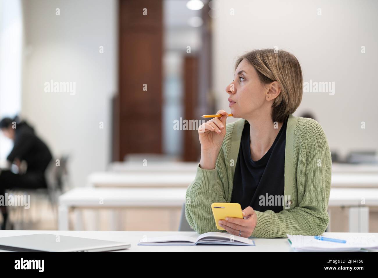 Donna pensiva studente maturo che guarda in lontananza mentre studia in biblioteca, disinteressato nello studio Foto Stock