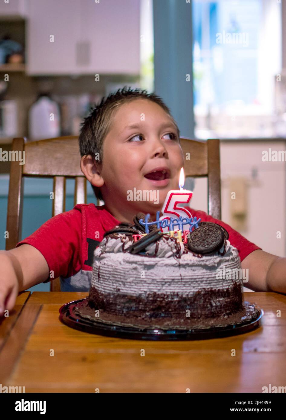 il ragazzo sorride mentre si siede prima di una torta bella il suo 5th compleanno Foto Stock