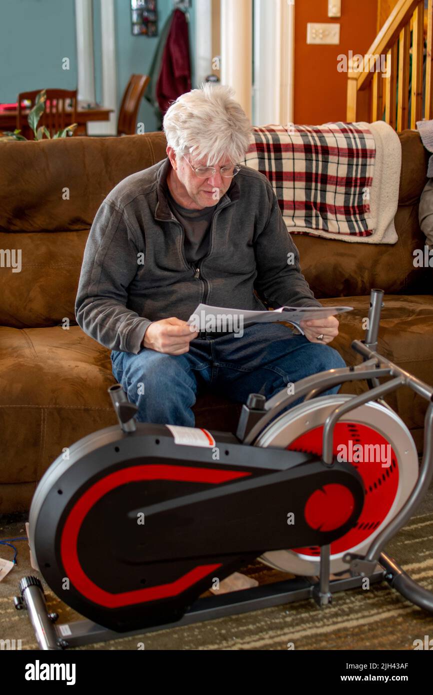 Un uomo più anziano legge le istruzioni su come assemblare una nuova bici da sforzo Foto Stock