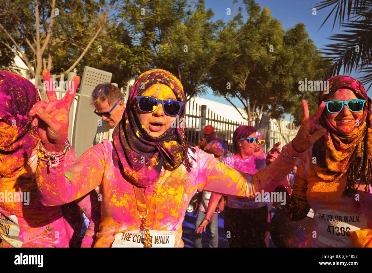 Ricoperta di polvere colorata, donna araba animata con Hijab e sfumature blu, regge due segnali di pace al Color Walk di Dubai, Emirati Arabi Uniti. Foto Stock