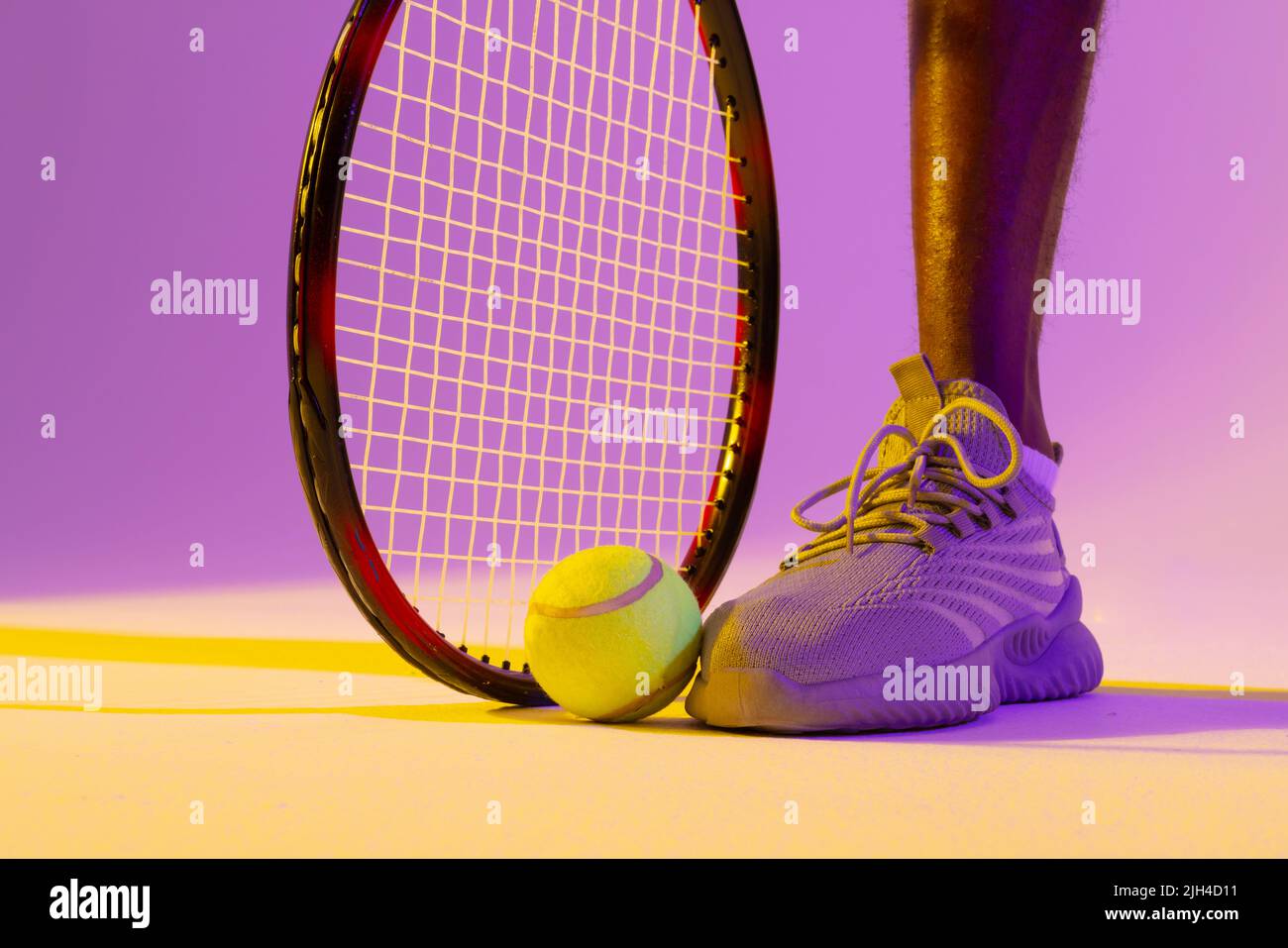 Immagine di una gamba di un giocatore di tennis maschile africano americano con illuminazione al neon viola e gialla Foto Stock