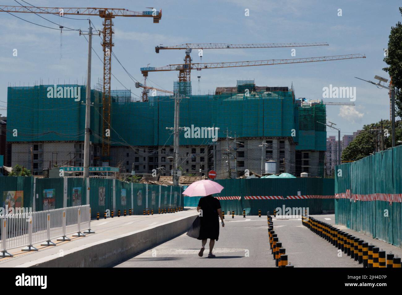 Una donna cammina vicino a un cantiere di edifici di appartamenti a Pechino, Cina, 15 luglio 2022. REUTERS/Thomas Peter Foto Stock