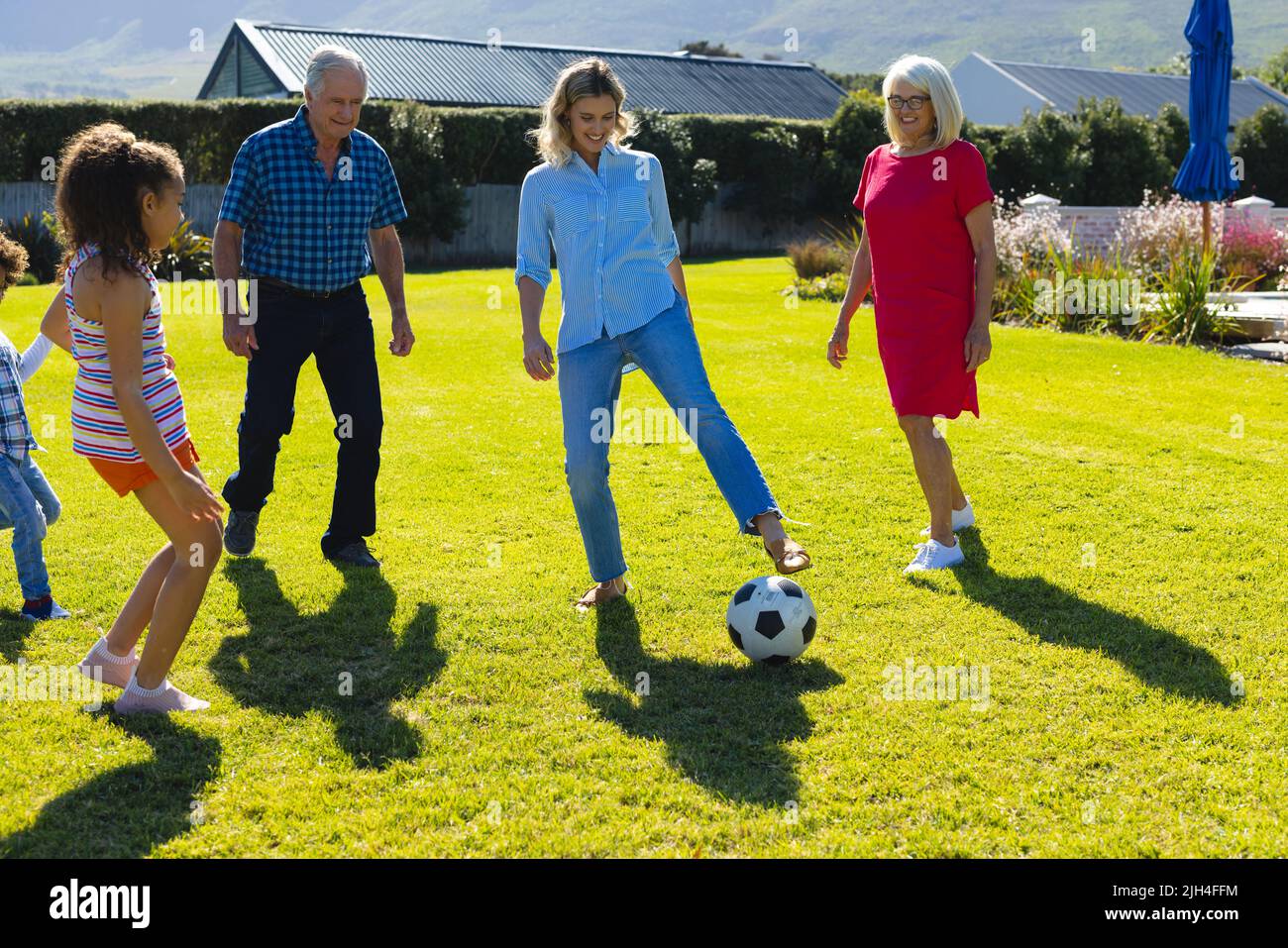 Felice famiglia multirazziale che gioca a calcio su terra erbosa in cortile in giorno di sole Foto Stock