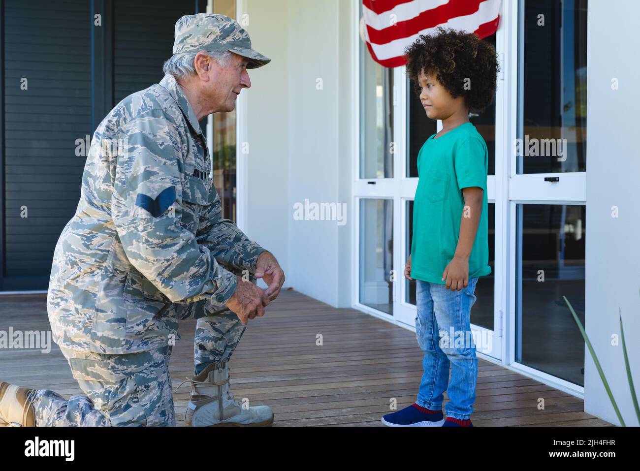 Nonno militare caucasico in abbigliamento camouflage guardando il nipote biraciale fuori casa Foto Stock