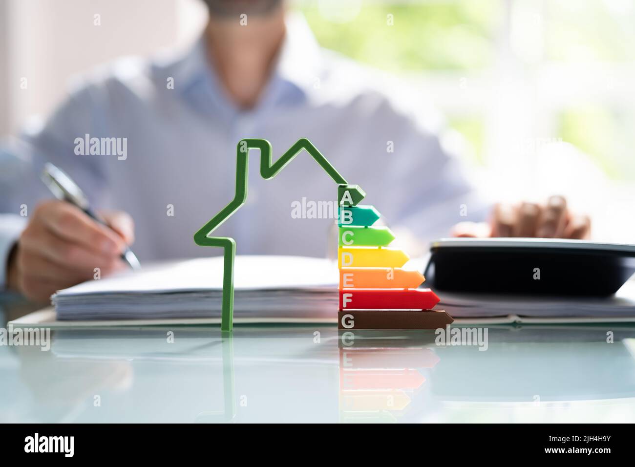 Close-up del modello di casa che mostra l'Efficienza Energetica tasso di fronte ai mediatori la mano utilizzando la calcolatrice Foto Stock