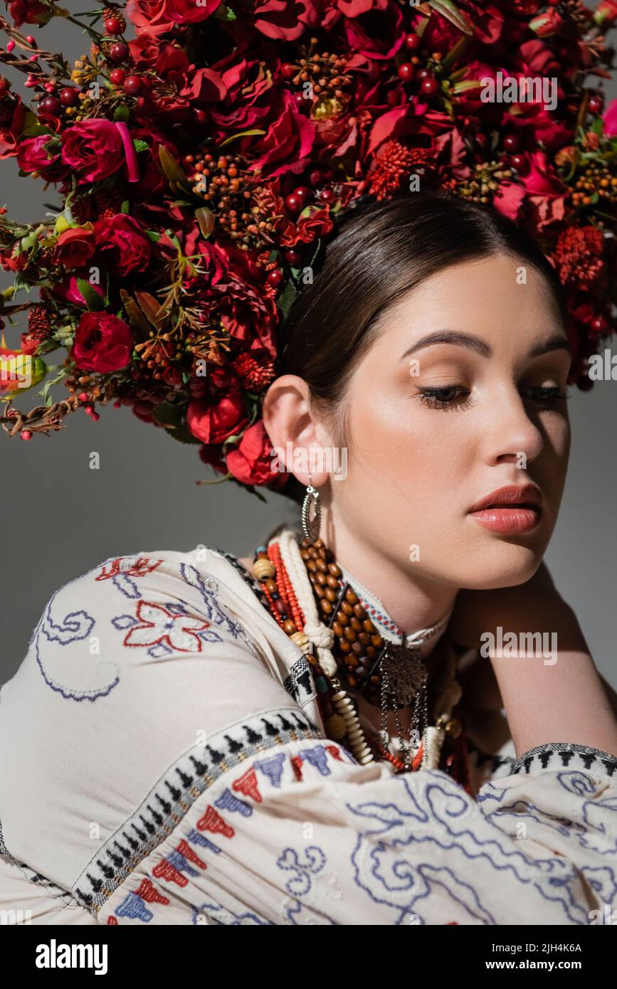 ritratto di graziosa donna ucraina in abiti tradizionali e corona floreale con bacche rosse isolate sul grigio Foto Stock