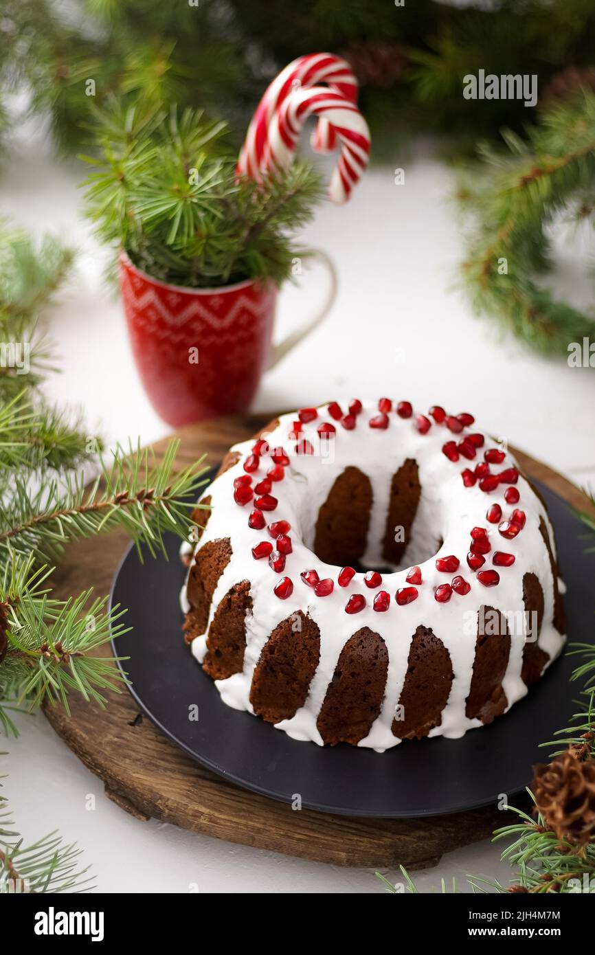 Cibo di Natale. Torta rotonda con glassa bianca. Cupcake con buco al centro con melograno. Rami di abete rosso verde sul tavolo. Vita morta. Dolci, dolci e dolci per il nuovo anno. Foto Stock