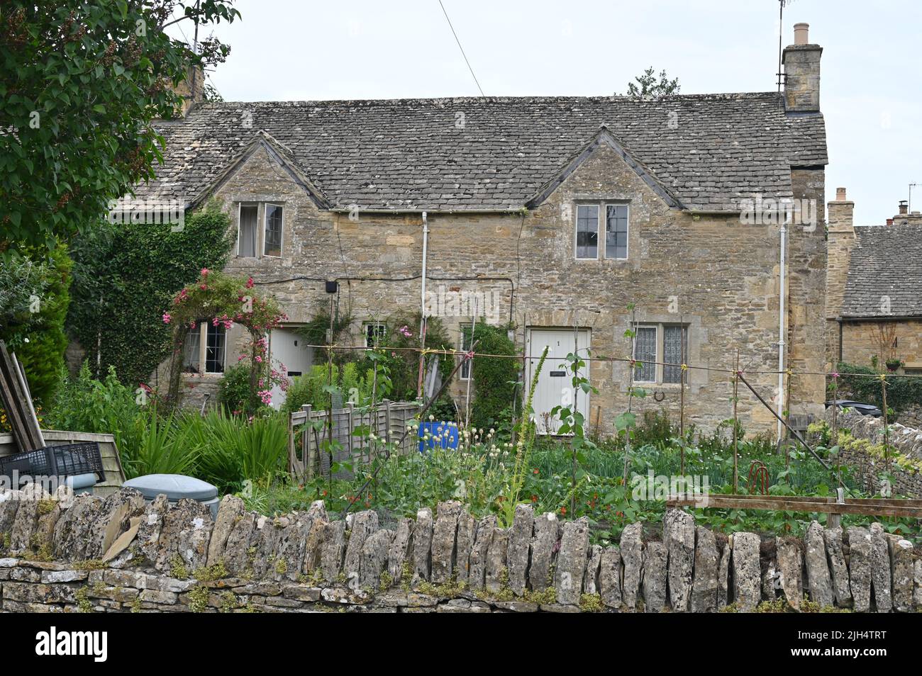 Un cottage nel villaggio Gloucestershire di Upper Slaughter mostra fuori il gaden anteriore che contiene una varietà di piante, tra cui piselli dolci in fiore Foto Stock