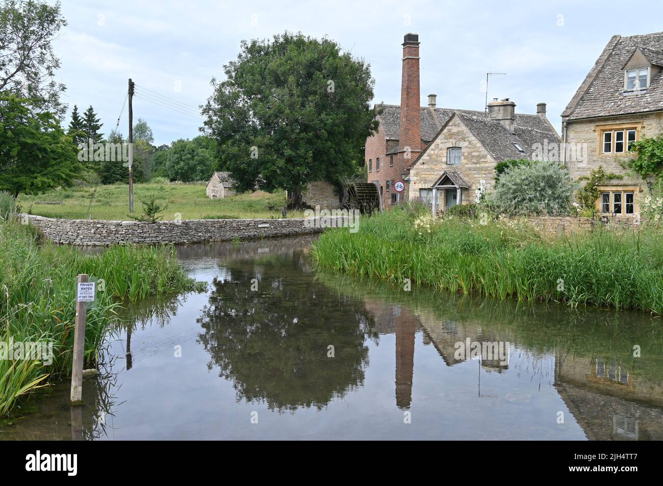 L'Old Mill sorge sul River Eye nel villaggio di Gloucestershire di Lower Slaughter. Il riflesso del mulino può essere visto nell'acqua Foto Stock