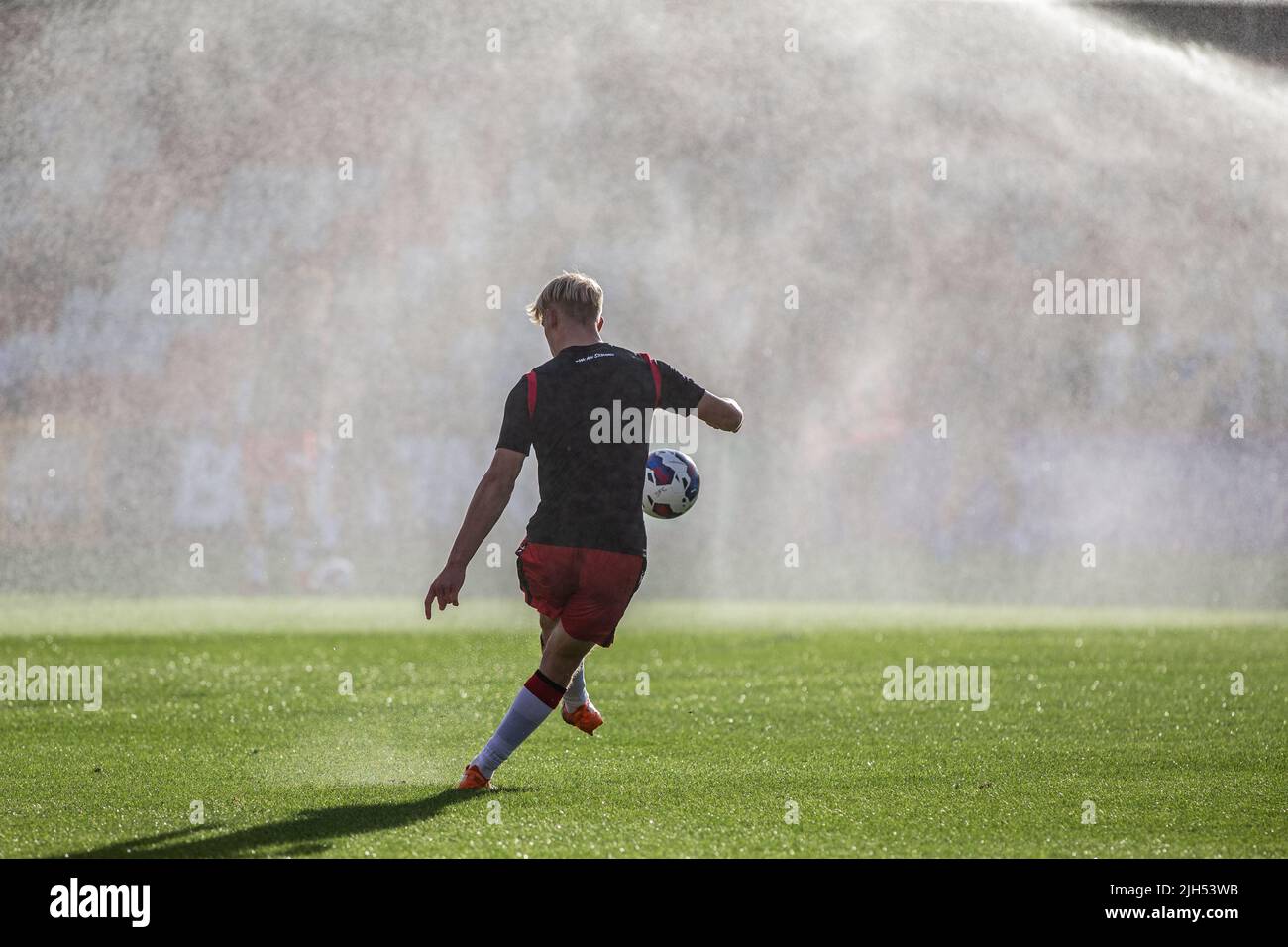 Il calcio si riscalda prima di una partita alla partita di campionato inferiore mentre gli sprinkler spruzzano acqua. Foto Stock