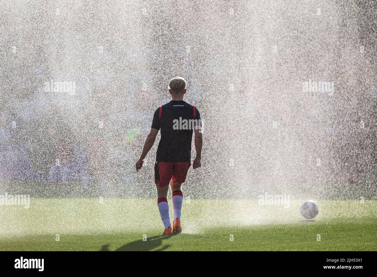 Il calcio si riscalda prima di una partita alla partita di campionato inferiore mentre gli sprinkler spruzzano acqua. Foto Stock