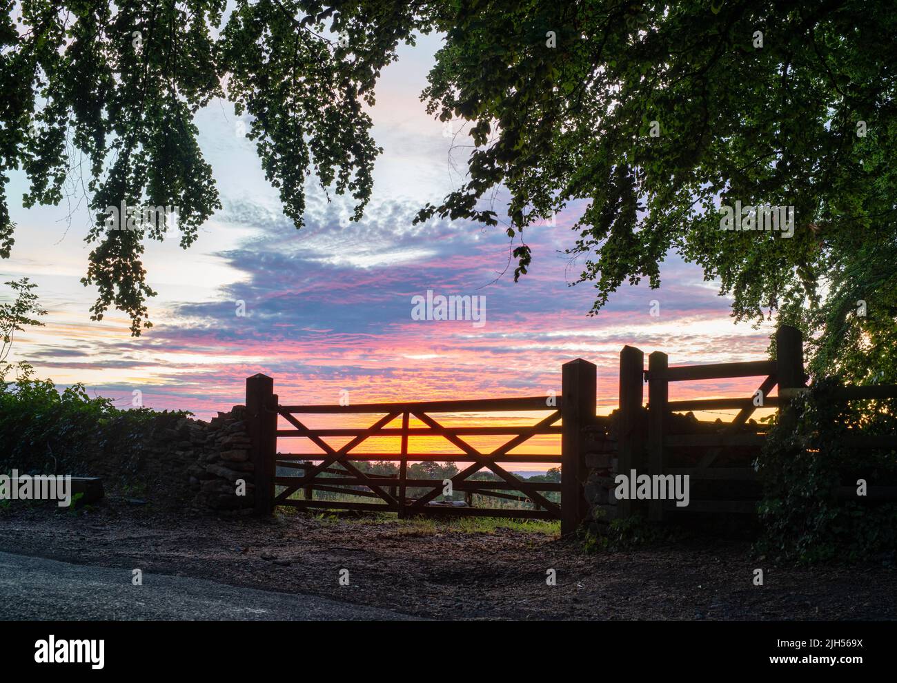 Silhouette cancelli fattoria all'alba in una mattinata d'estate nella campagna inglese. Bourton sulla collina, Cotswolds, Oxfordshire, Inghilterra Foto Stock