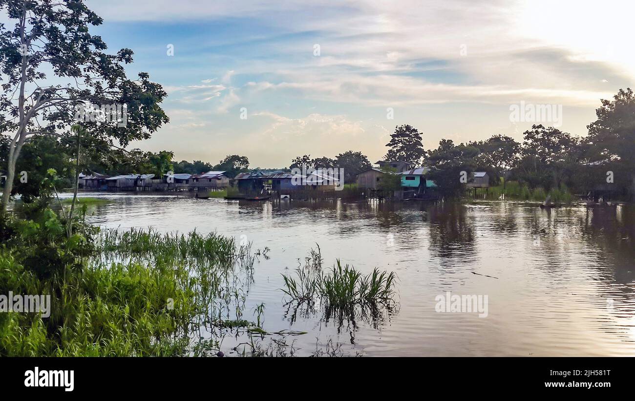 Case di palafitte costruite su pali sopra l'acqua marrone del fiume Amazzonia. Favela baraccopoli di tribù indiane locali. Scarsa protezione degli alloggi contro le alluvioni Foto Stock