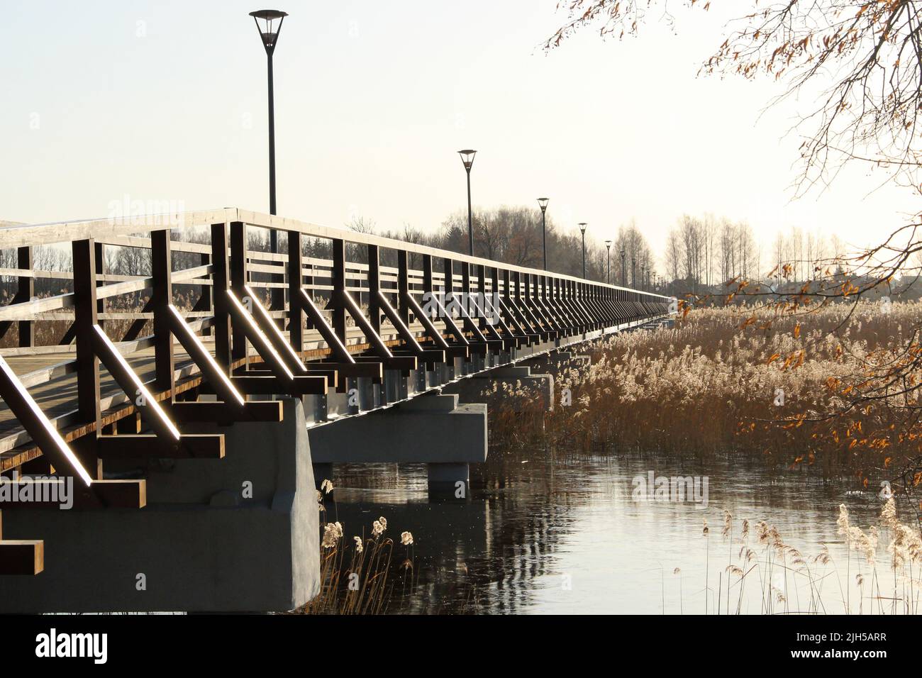 Un ponte di legno attraversa il lago. Camminando sulla passerella durante mezzogiorno. Paesaggio sul lago e sul ponte in una giornata di sole. Foto Stock