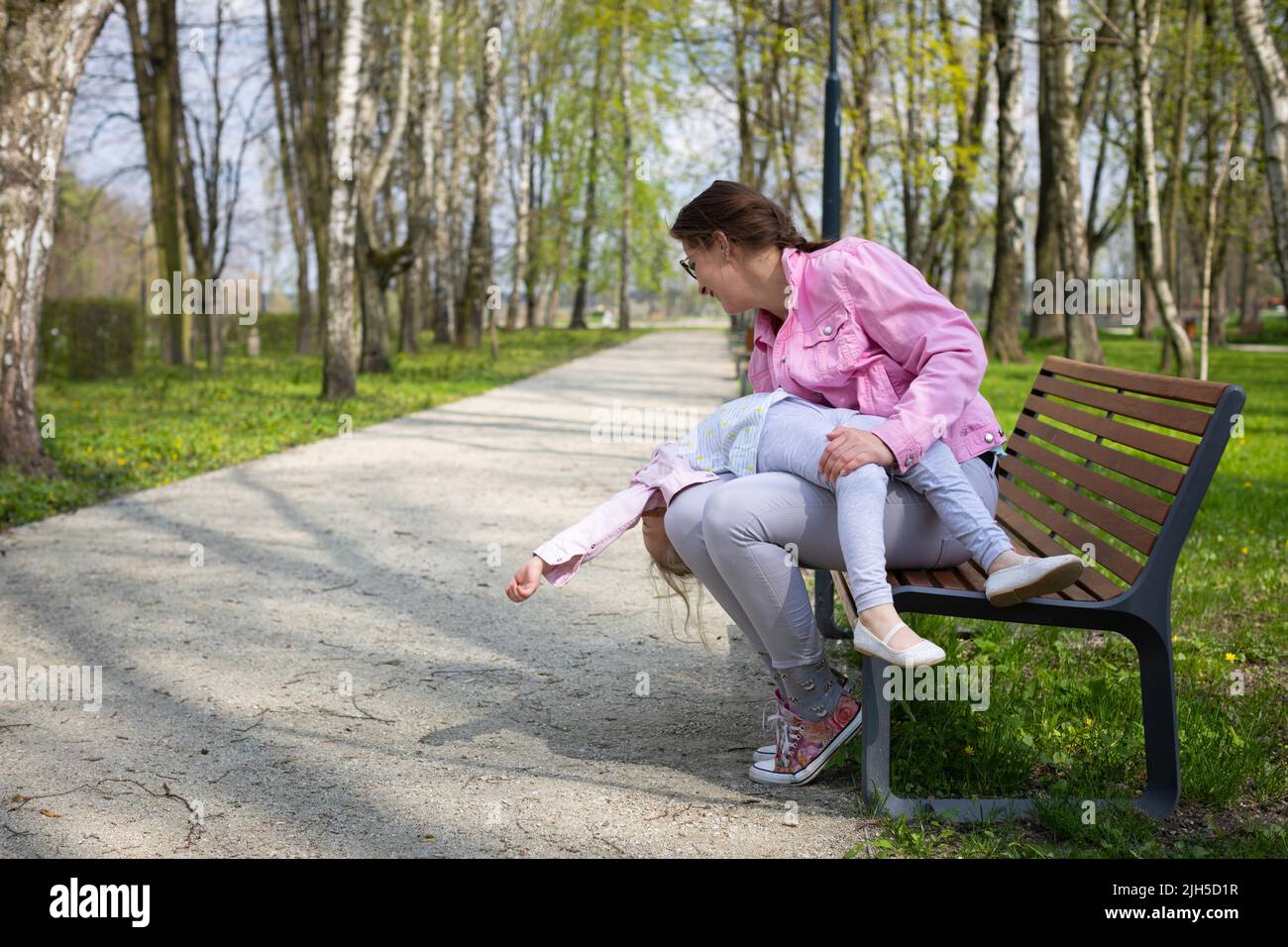 Madre e figlia che si imbrogliano mentre si siedono su una panchina in un parco cittadino. Foto Stock