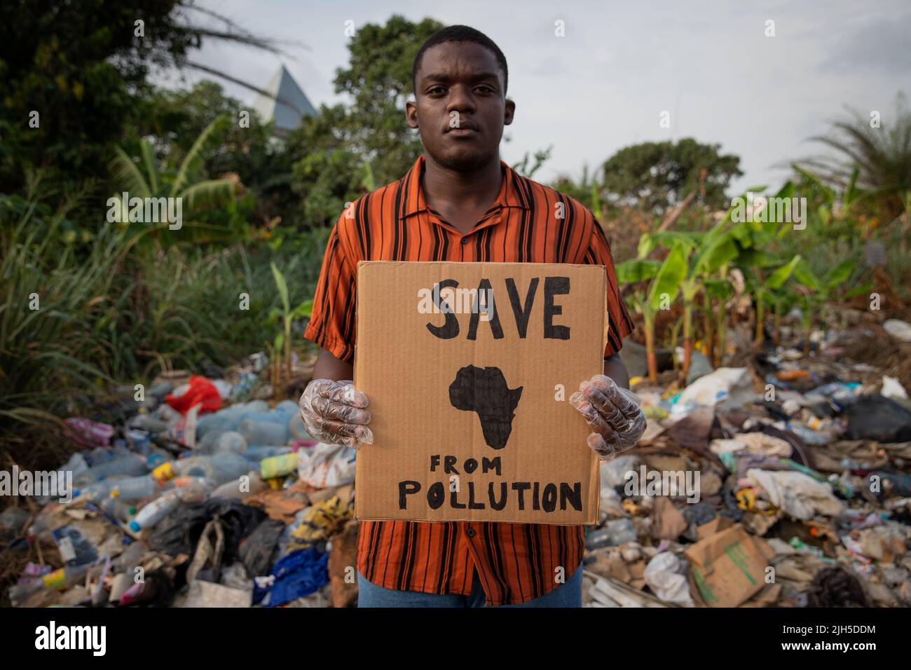 Un ragazzo ha un cartello "salvare l'Africa dall'inquinamento" e si trova in una discarica illegale. Protesta contro l'inquinamento in africa Foto Stock