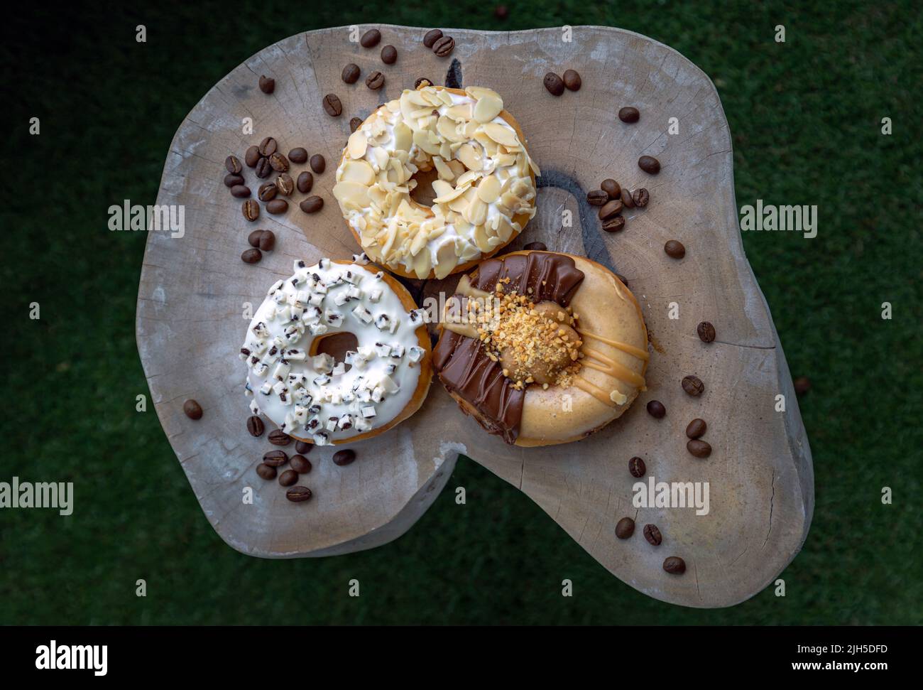 Tre ciambelle ricoperte di biscotti e crema, Almendra e burro di arachidi di cioccolato su tagliere di legno su sfondo scuro. Il concetto di Delicious Foto Stock