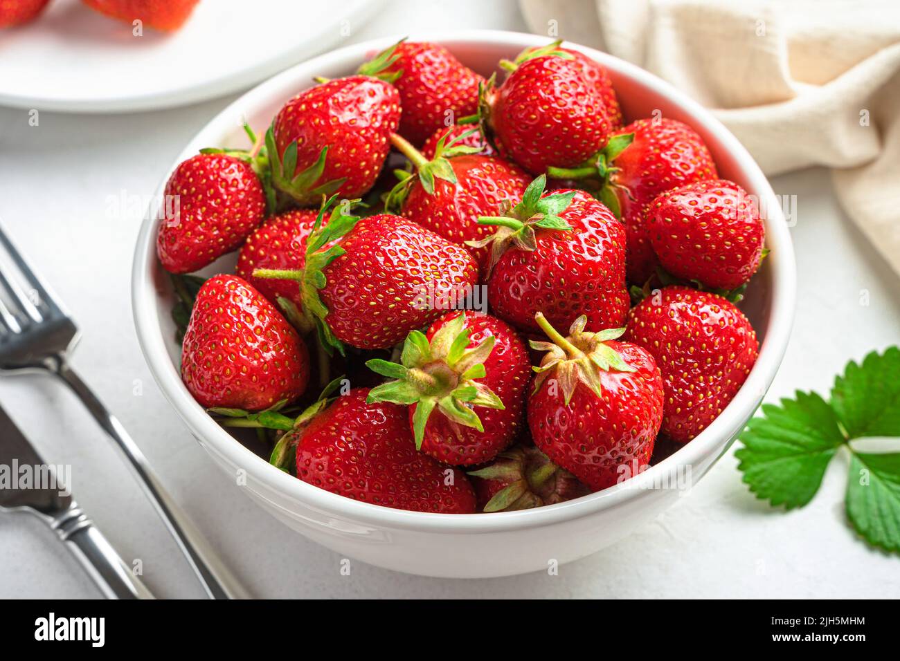 Fragole in un recipiente bianco su sfondo chiaro. Foto Stock
