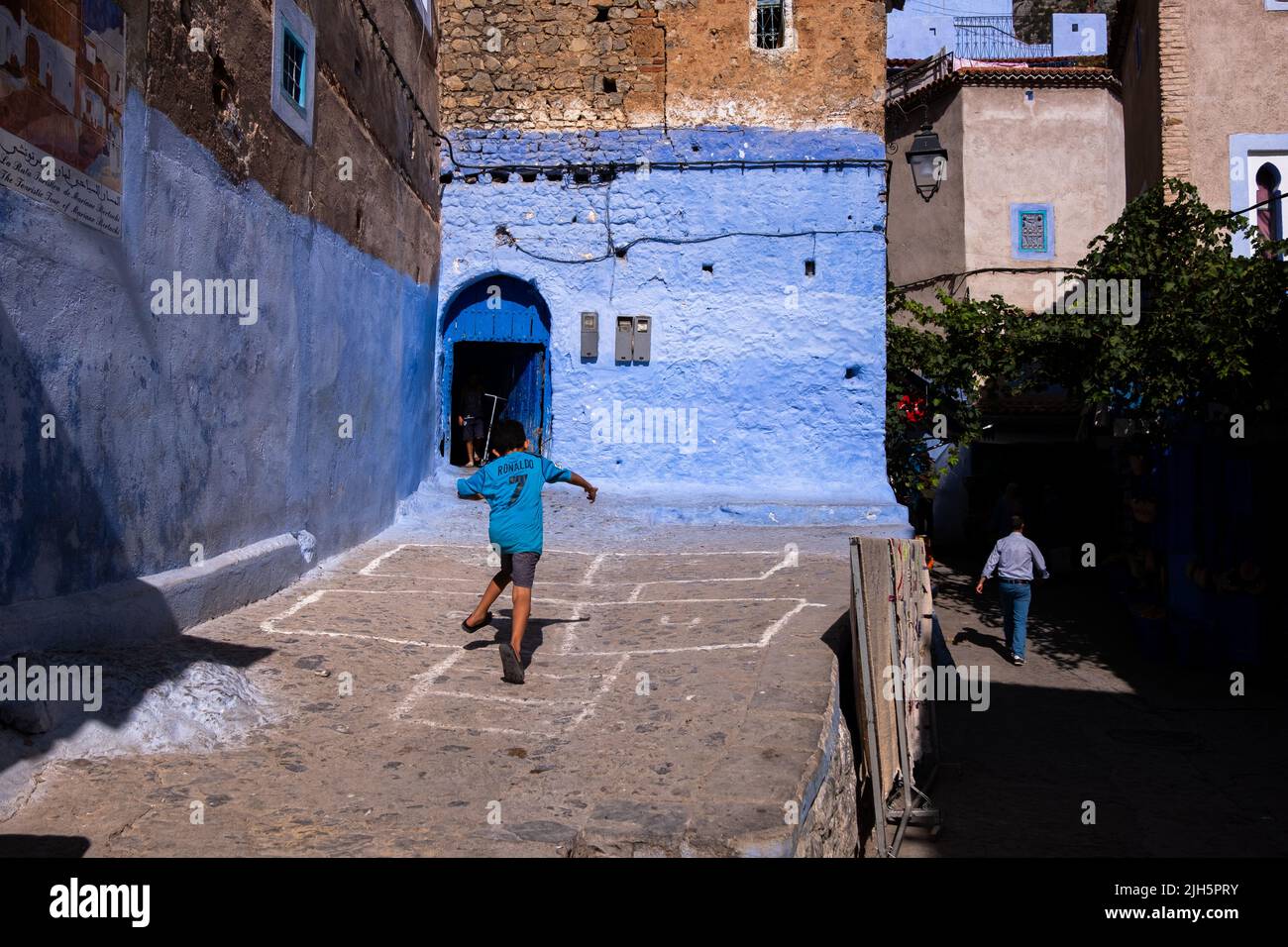 Bambino che gioca in una strada a Chefchaouen mentre un uomo cammina al buio Foto Stock