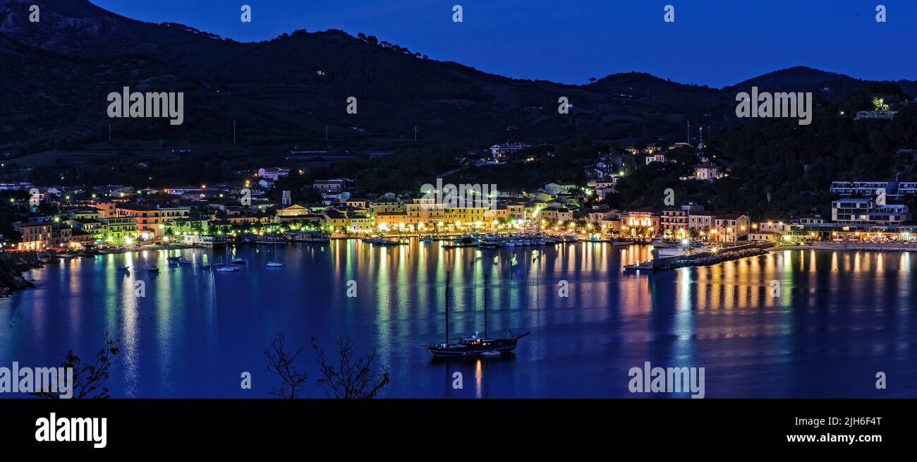 Vista panoramica di Porto Azzurro con passeggiata del porto illuminata durante l'ora blu, Porto Azzurro, Elba, Toscana, Italia Foto Stock