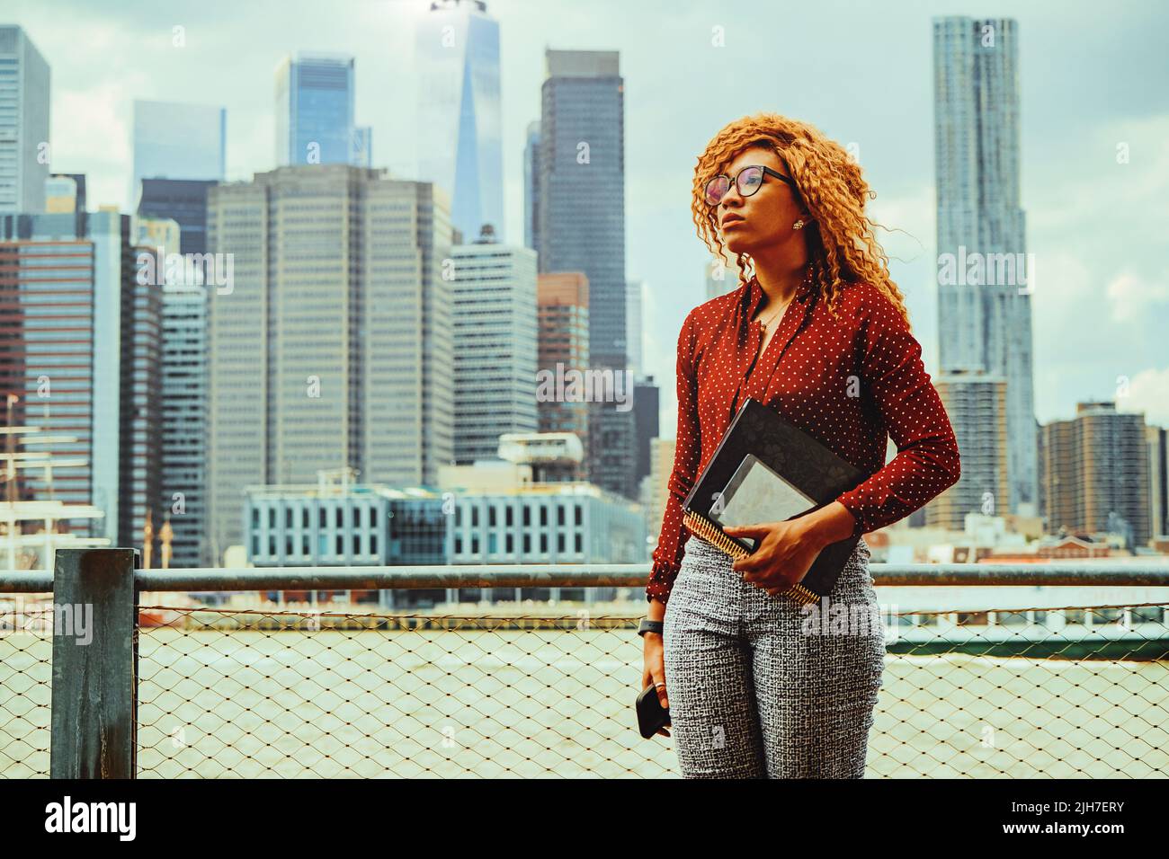 Ritratto pensieroso giovane imprenditore adulto donna millennial con occhiali e capelli afro guardando via lo spazio copia con Downtown Manhattan New York skyline grattacielo dietro il fiume Hudson Foto Stock