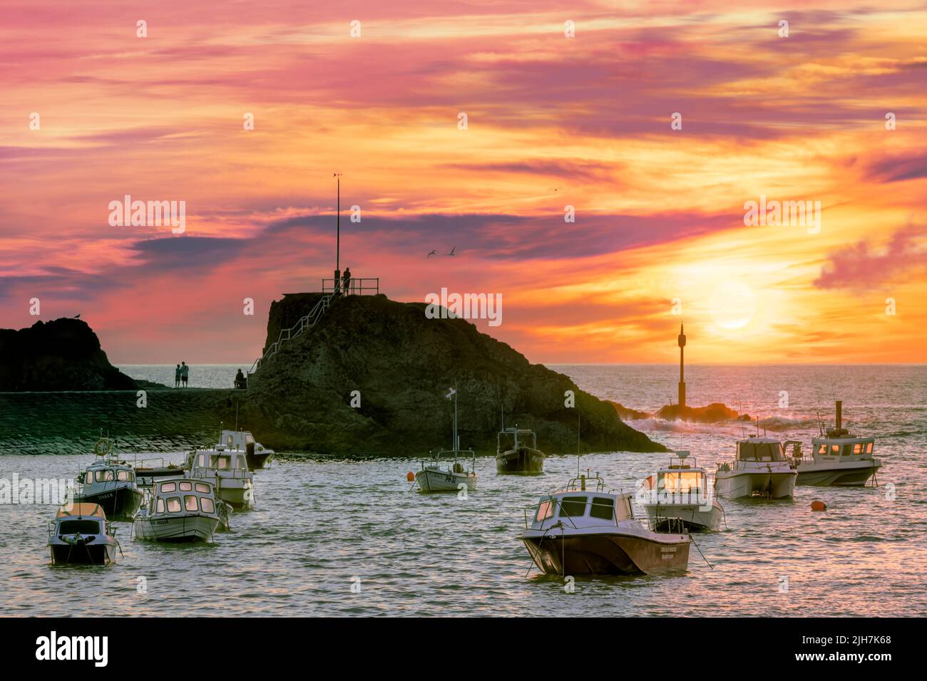 Dopo una giornata molto calda di luglio sulla costa della Cornovaglia, il cielo si trasforma in sfumature di rosa e arancione, mentre le persone si riuniscono per guardare il sole tramontare attraverso la foschia sul Foto Stock