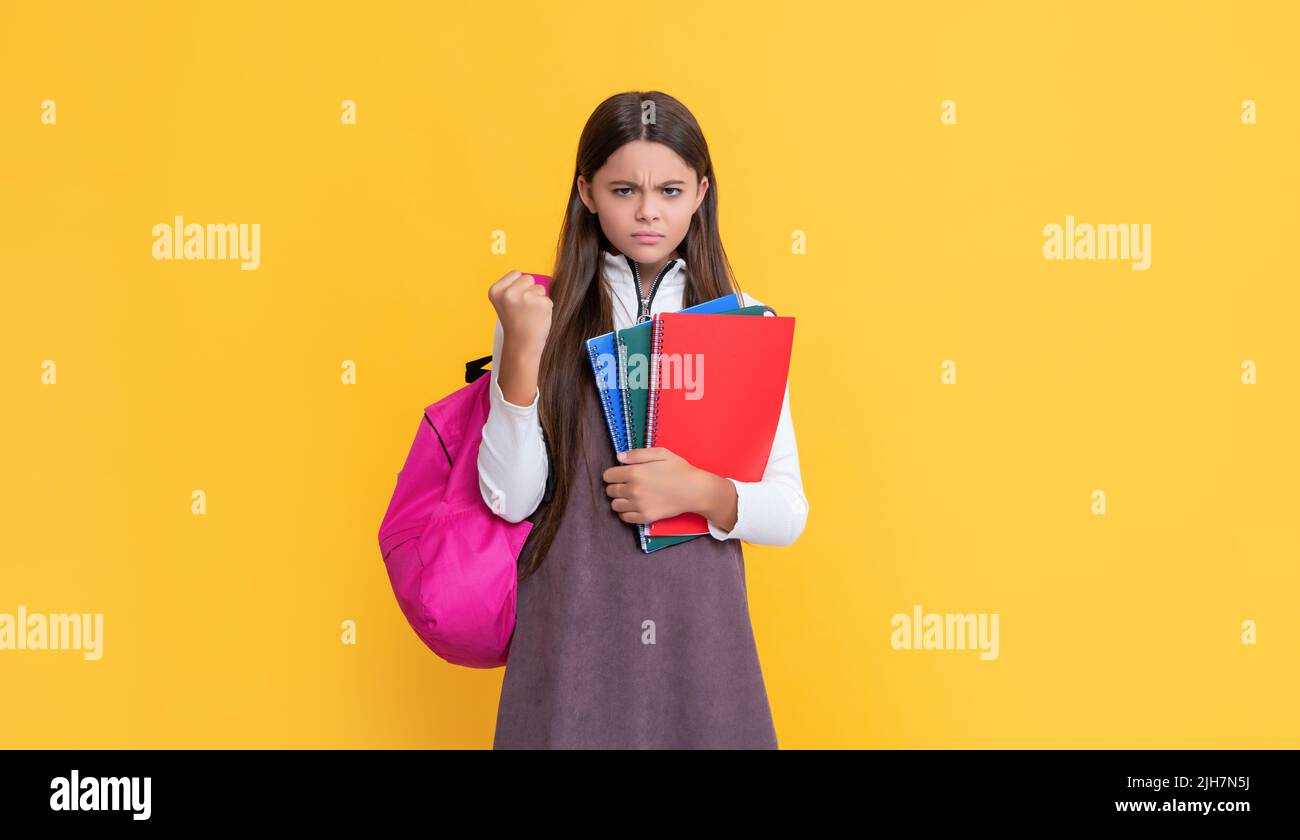 bambino arrabbiato con zaino scuola e libro degli esercizi su sfondo giallo Foto Stock