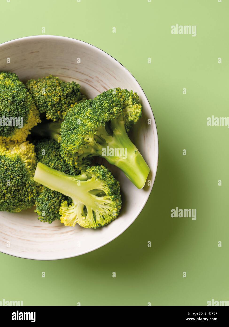 I broccoli crudi si florets interi e dimezzati in una ciotola su sfondo verde pastello. Dieting disintossicante a basso contenuto calorico e cibo vitaminico vegetariano. Foto Stock