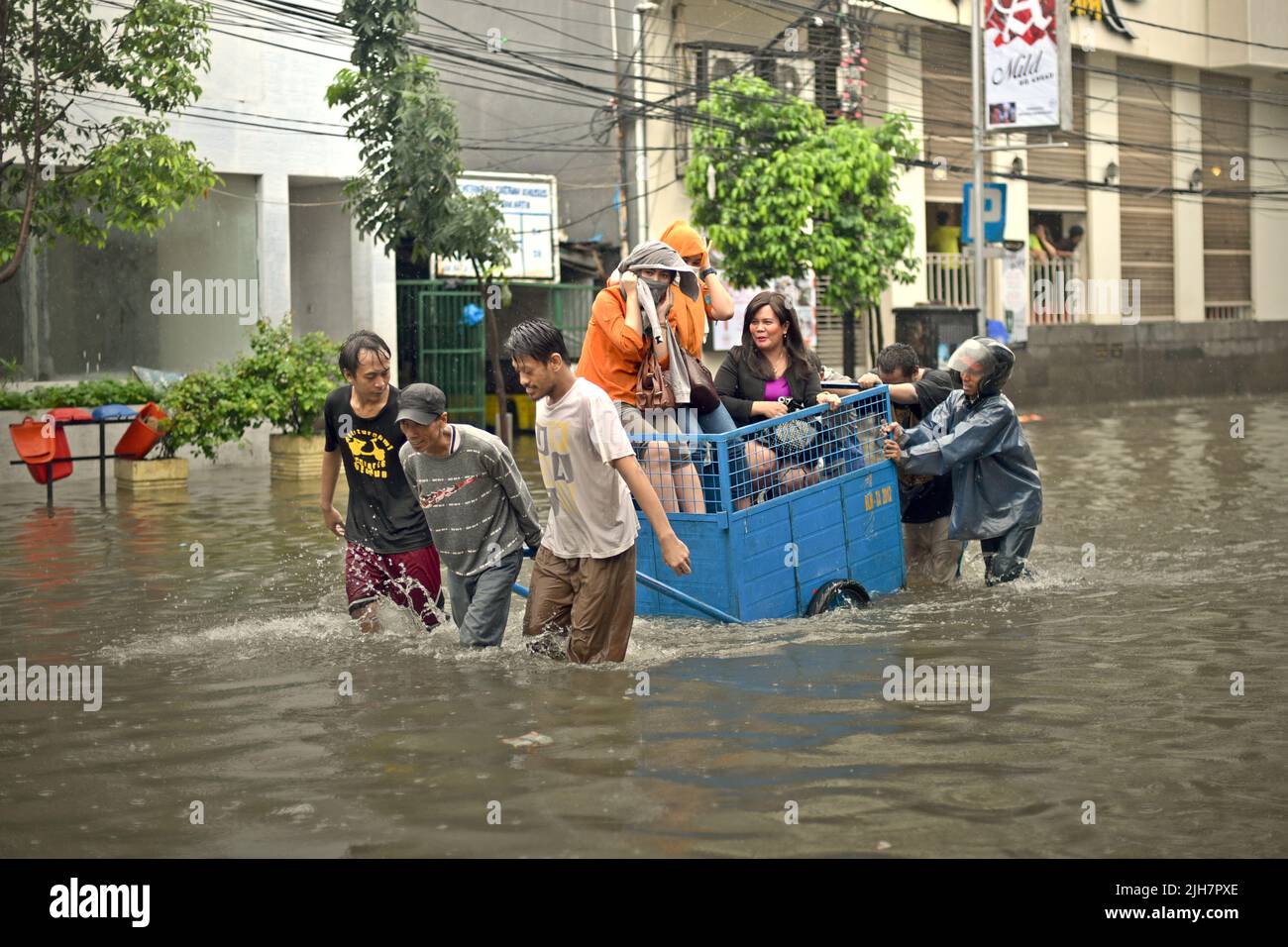 Uomini che aiutano le donne a viaggiare attraverso una strada allagata da un carro a Giacarta, dopo una pioggia continua ha lasciato l'area del centro della capitale indonesiana inondato. Foto Stock