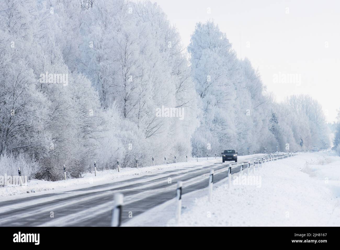 Un'auto buia che guida su un'autostrada circondata da alberi gelidi e da un paesaggio innevato Foto Stock