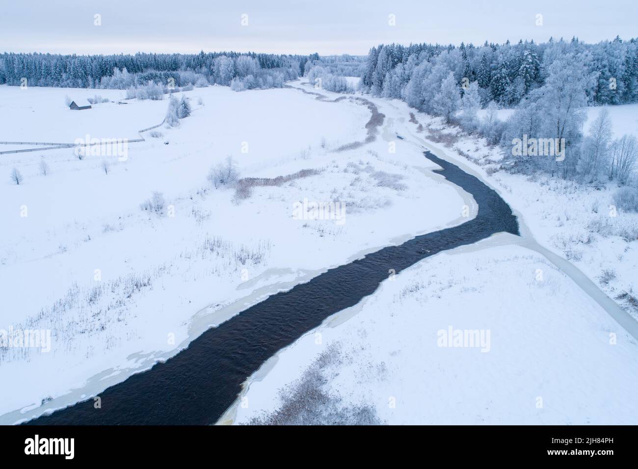 Aereo di un paesaggio rurale ghiacciato e innevato con un fiume aperto in inverno estone, Nord Europa. Foto Stock