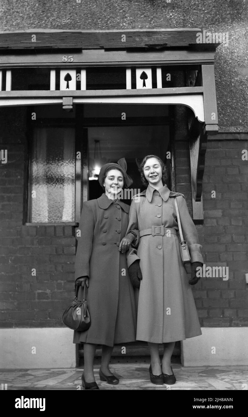 1940s, storica, due eleganti giovani donne nei loro cappotti, guanti e borse, in piedi per la loro foto fuori dall'ingresso di una casa, sotto una tenda decorativa porta incorniciata in legno o sovrahang, Inghilterra, Regno Unito. Foto Stock