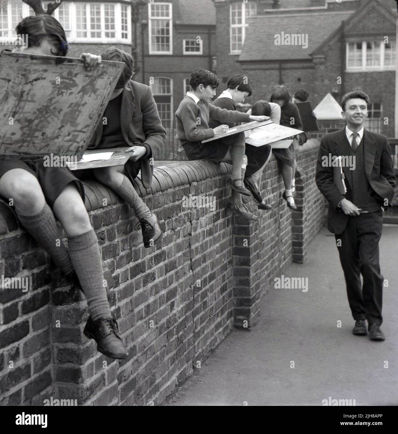 1960s, storico, bambini della scuola elementare seduti sul muro del parco giochi, disegno esterno, insegnante passeggiando, Inghilterra, Regno Unito Foto Stock
