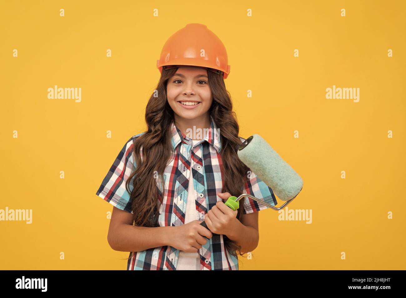 bambino felice con capelli ricci in costruzione casco tenere rullo vernice, pittura Foto Stock